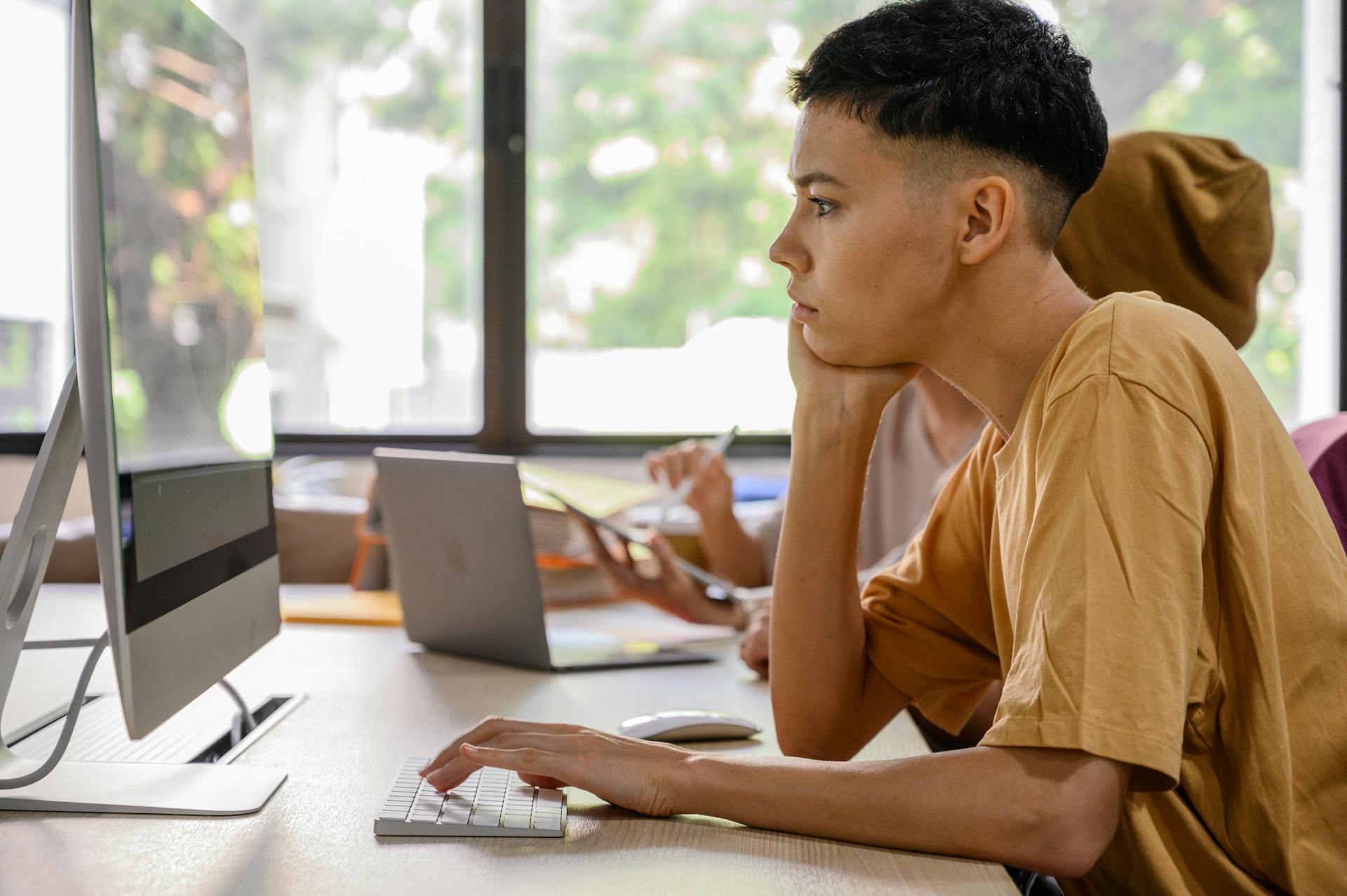 Two people engaged in focused work at an office with computers and natural light.