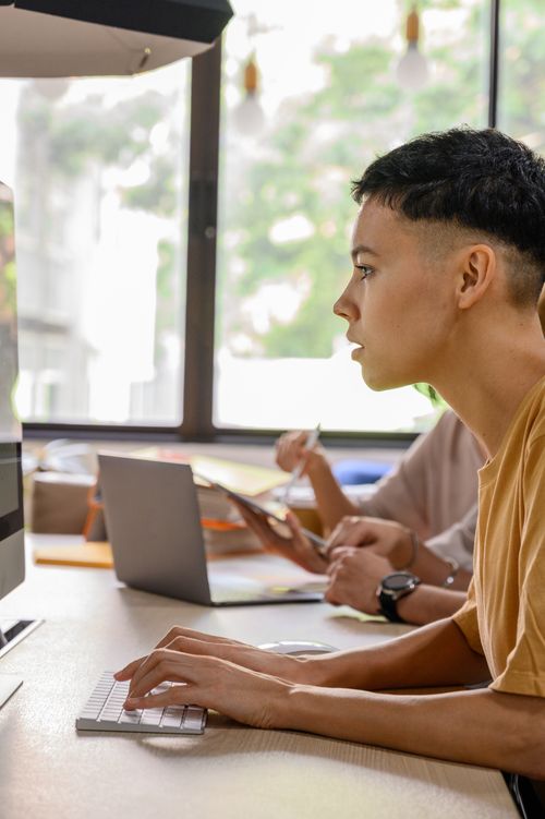 Free A young adult working at a desk with a computer in a modern office environment. Stock Photo