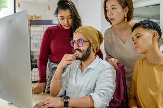 Four colleagues gathered around a computer screen engaging in a collaborative discussion in an office.