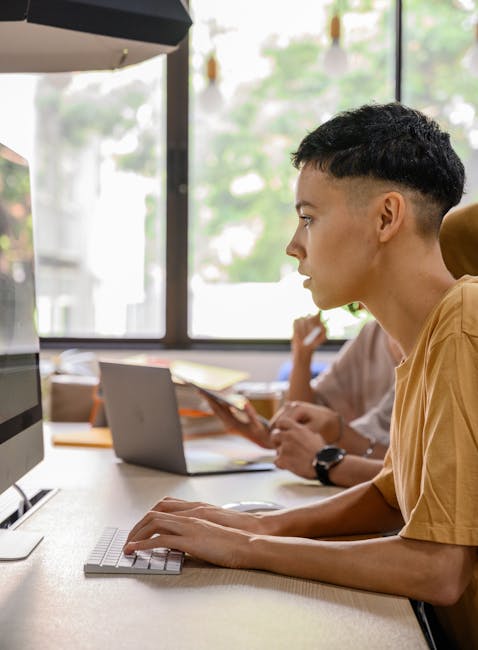 Teenager attentively working on desktop computer in a bright, modern office environment.