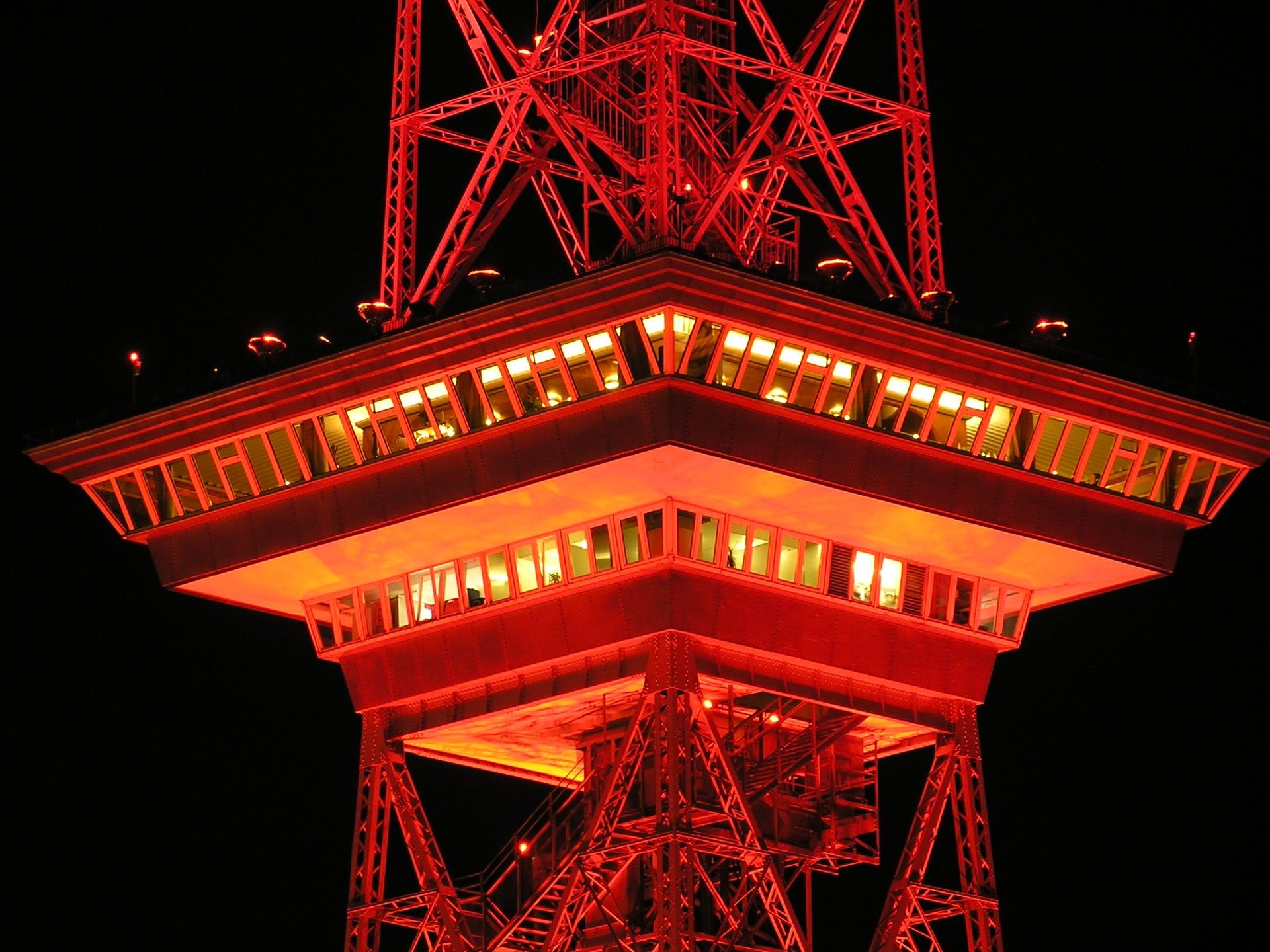 A vividly illuminated red tower structure casting light in the night sky. Architectural marvel.