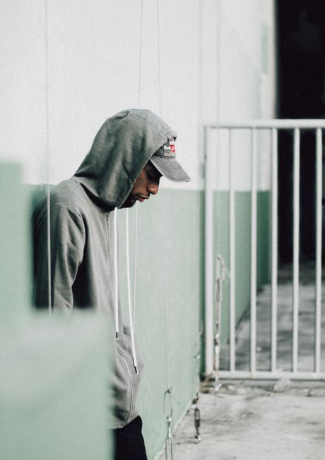 A man in a gray hoodie leans against a green wall, reflecting a stylish urban scene.