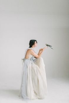 在光线柔和的工作室里，一位时尚的新娘穿着飘逸的白色连衣裙，抱着一只鸟