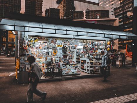 Small bookstore with a lot of books and magazines  located near busy road and pavement with pedestrians