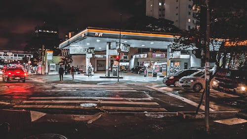 Cars driving down asphalt busy roadway with crossing near modern illuminated gas station