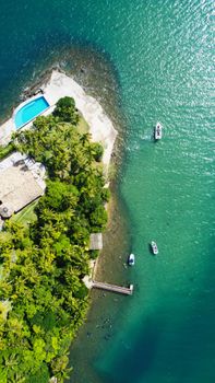 Picturesque drone view of tropical island in turquoise sea with floating boats on sunny summer day
