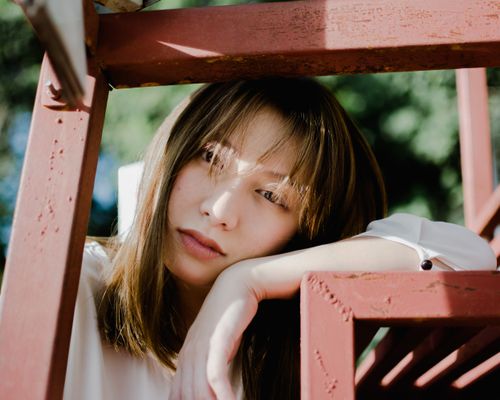 Free A pensive Asian woman resting her arm on a red structure outdoors in sunlight. Stock Photo
