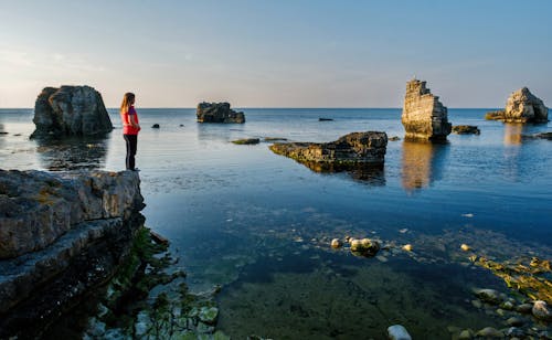 Anonymous female tourist admiring rocky ocean at sundown