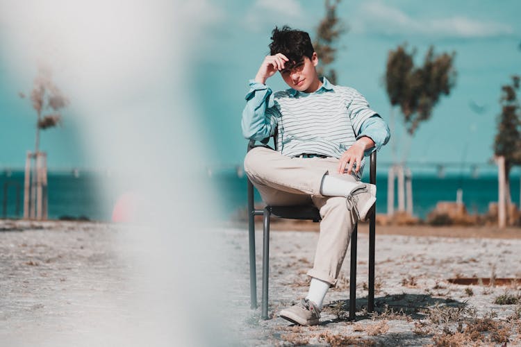 Relaxed Teen Boy Sitting On Chair Near Sea