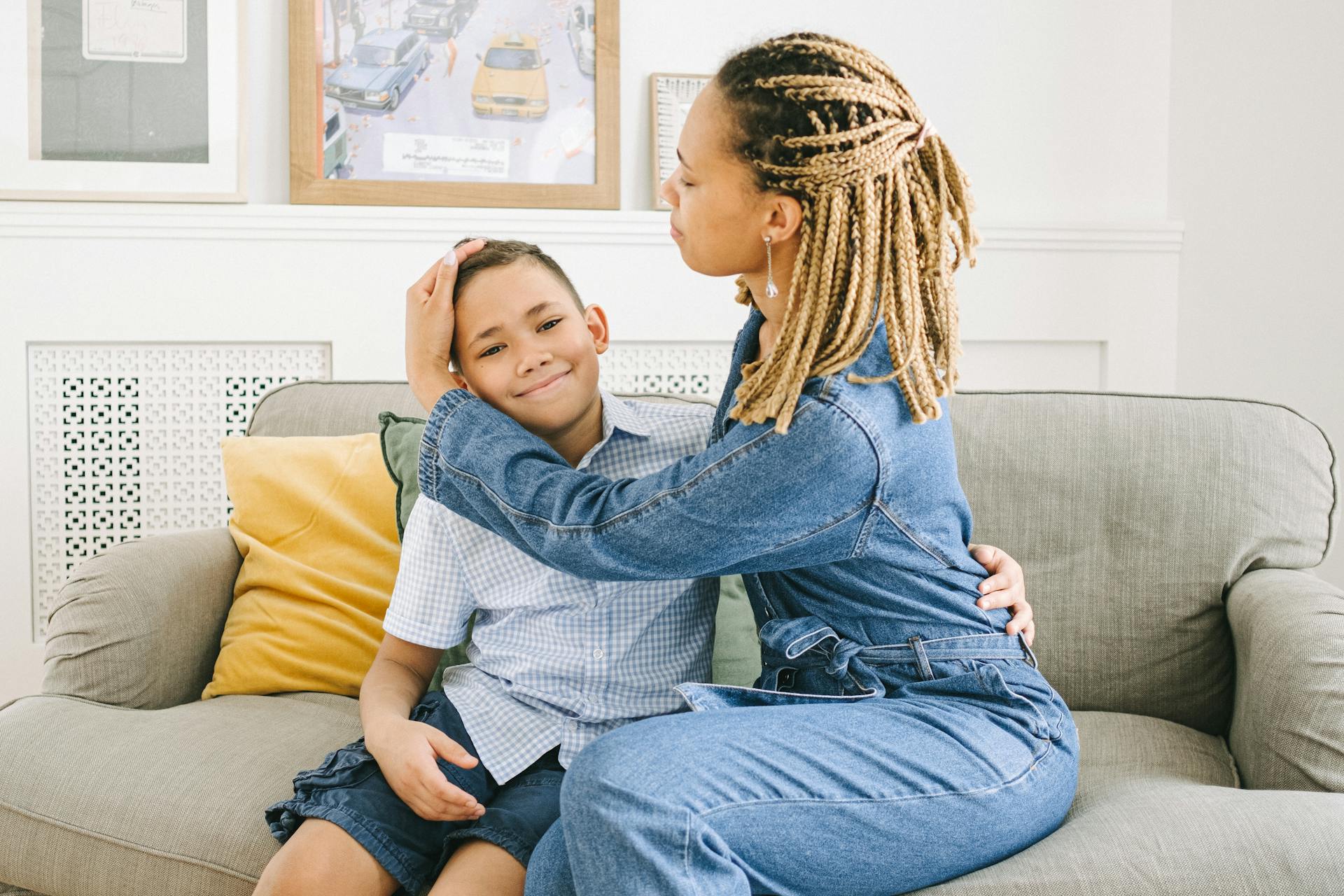 A woman with braids embraces her son on a sofa, creating a warm family moment.