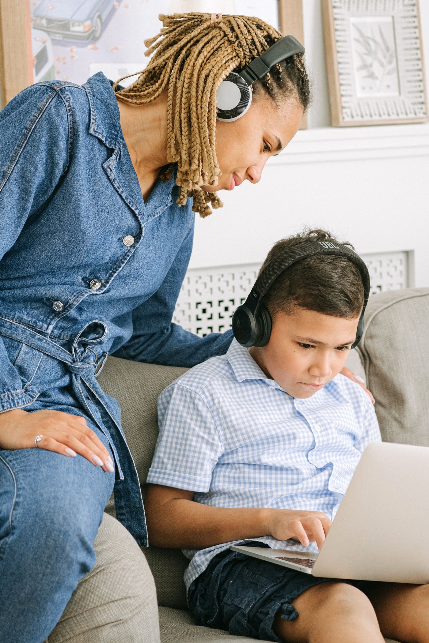 A Black mother supporting her son during online learning at home with a laptop.