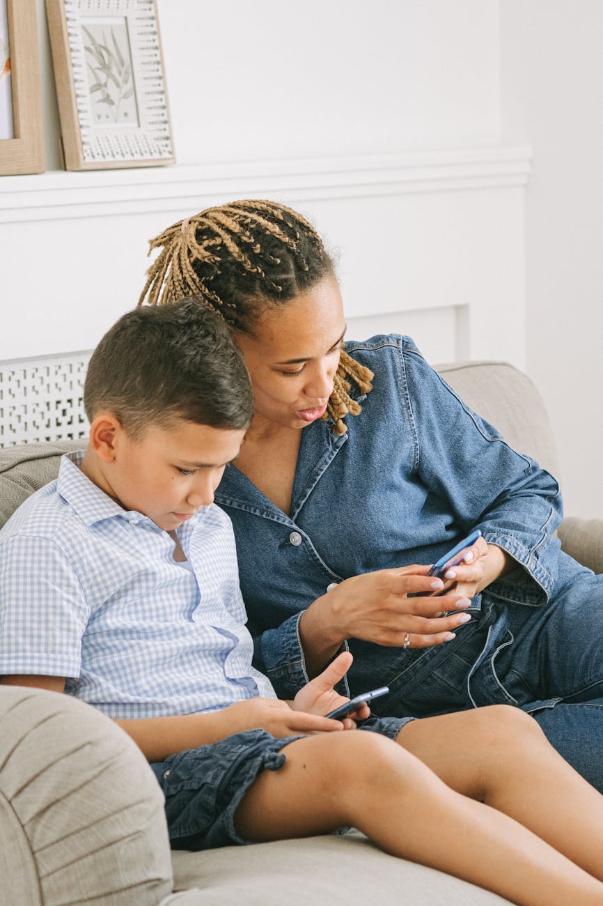 A mother and her son sit on a sofa, engaged with their smartphones indoors.