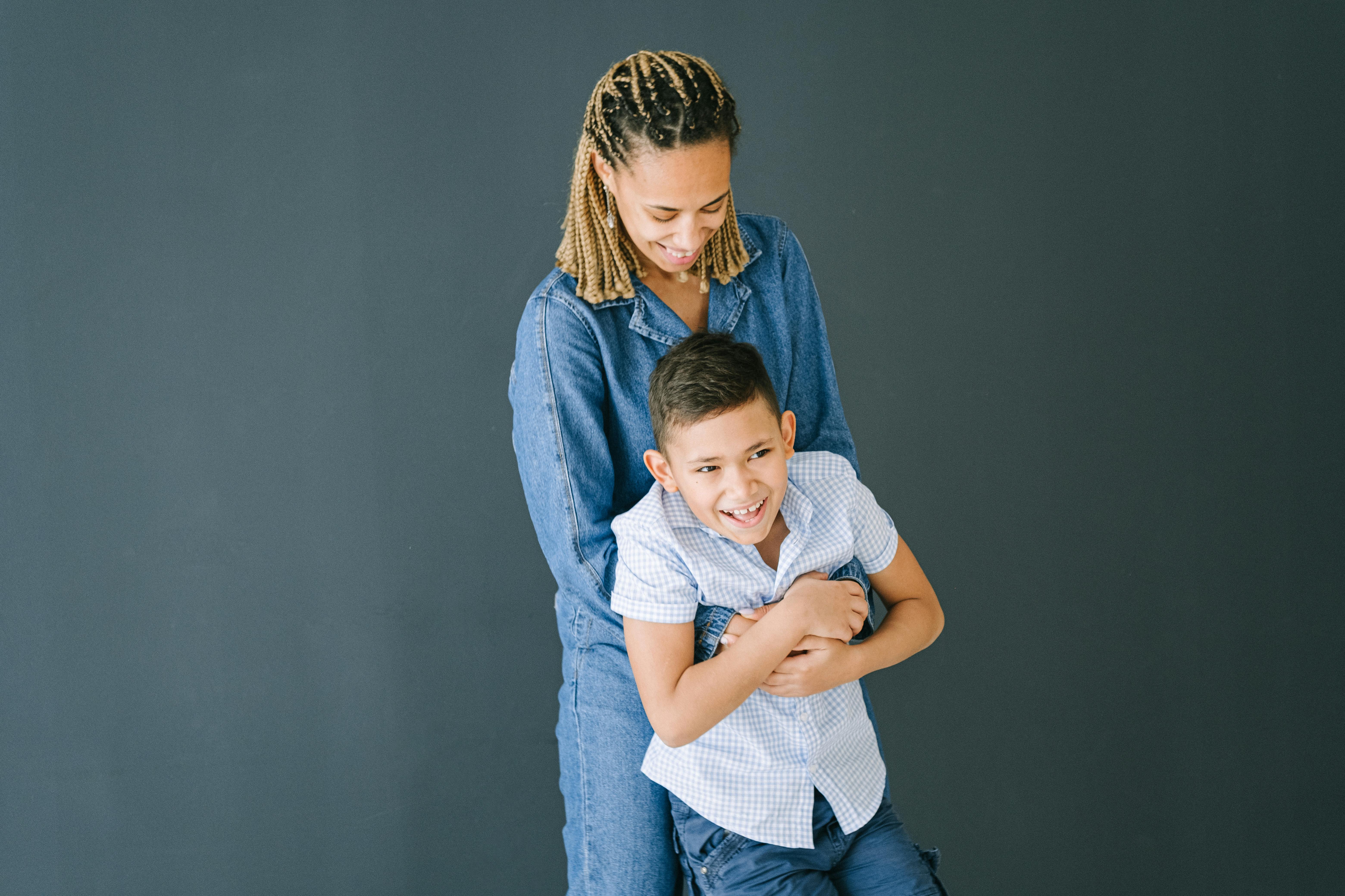 woman in demin clothing hugging young boy from behind