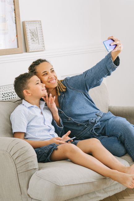 A joyful mother and son taking a selfie on a sofa, capturing a moment of togetherness and happiness indoors.