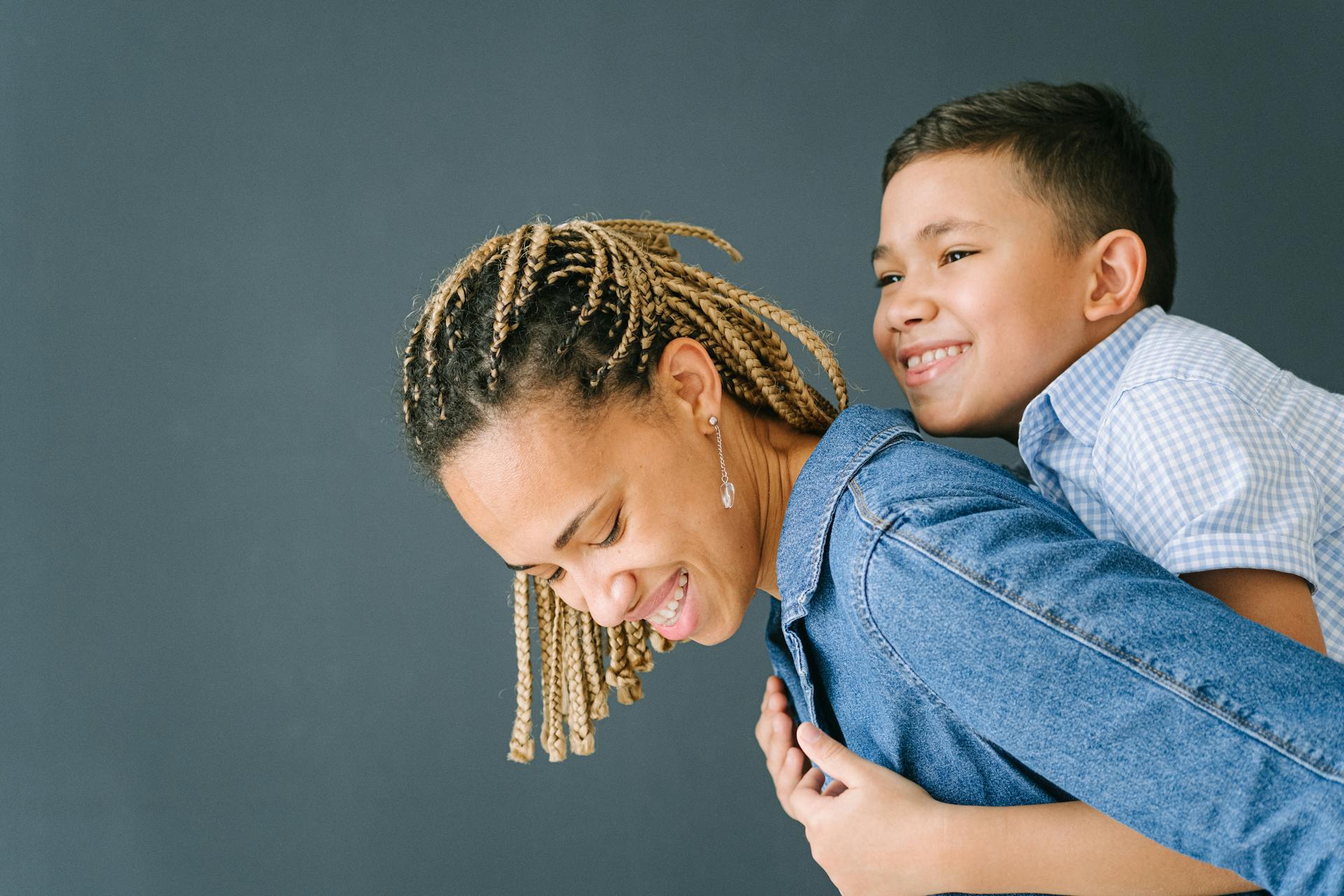 A mother with braids carrying her smiling son on her back, expressing joy and bonding.
