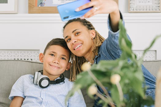 Smiling mother and son capturing a selfie together indoors on a cozy couch.