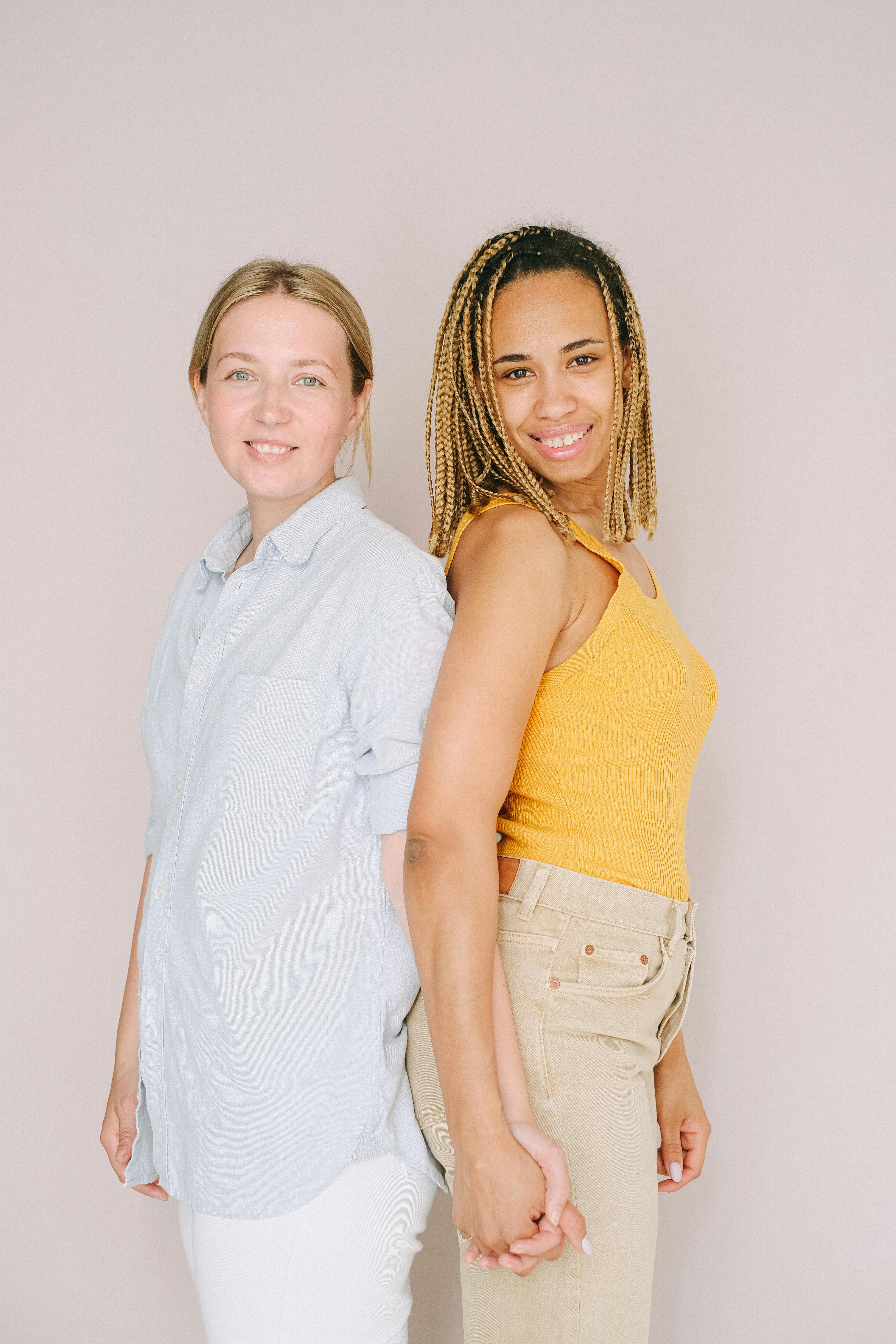 Two women standing back-to-back holding hands, showcasing unity and love.