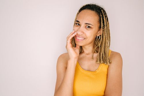 Free Portrait of a woman with braided hair and a yellow tank top, smiling against a white background. Stock Photo