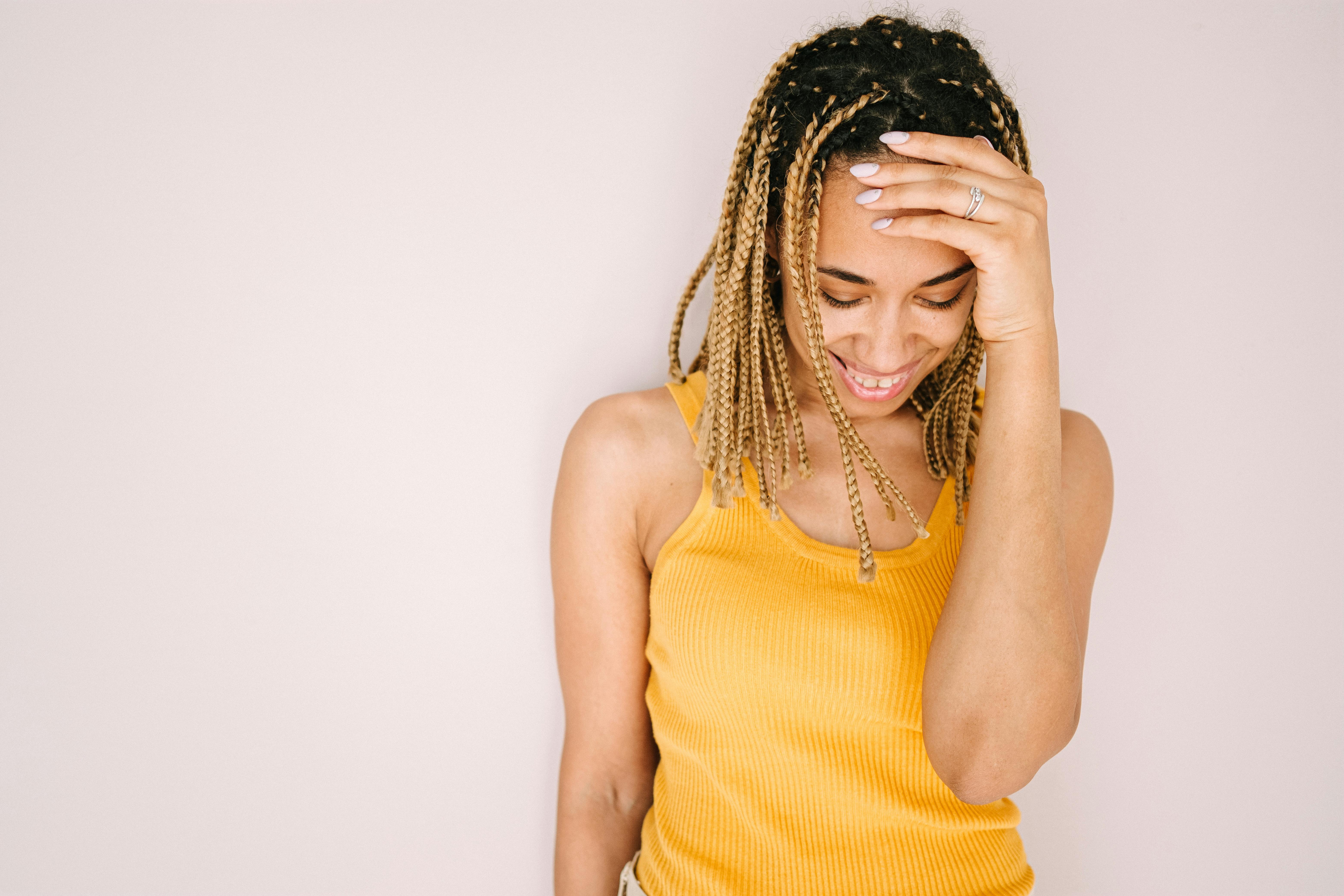 A joyful young woman in a stylish yellow top, smiling and touching her hair.