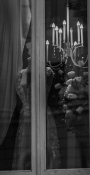 Black and white of artificial ma mannequin and chandelier with burning lamps through window