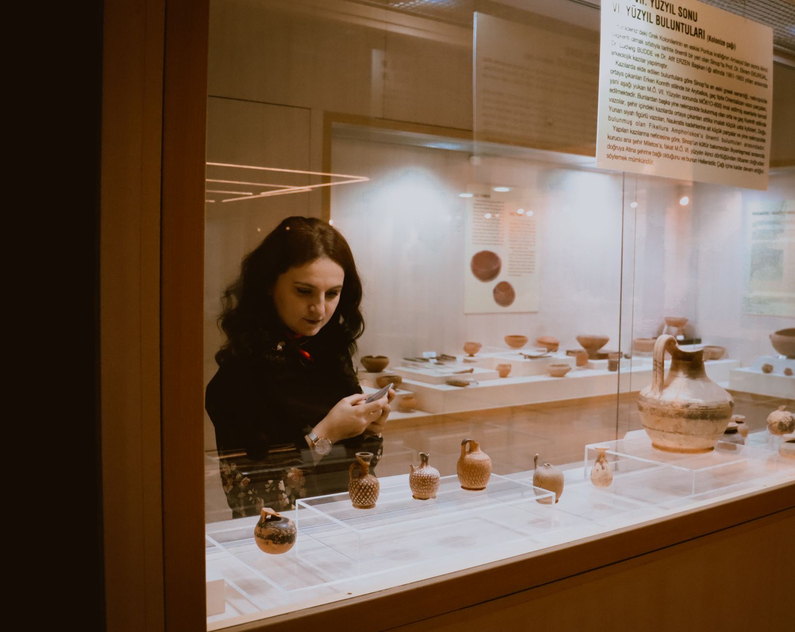 Young curious female with long hair visiting museum and comparing ancient fragile ceramic exhibits near window