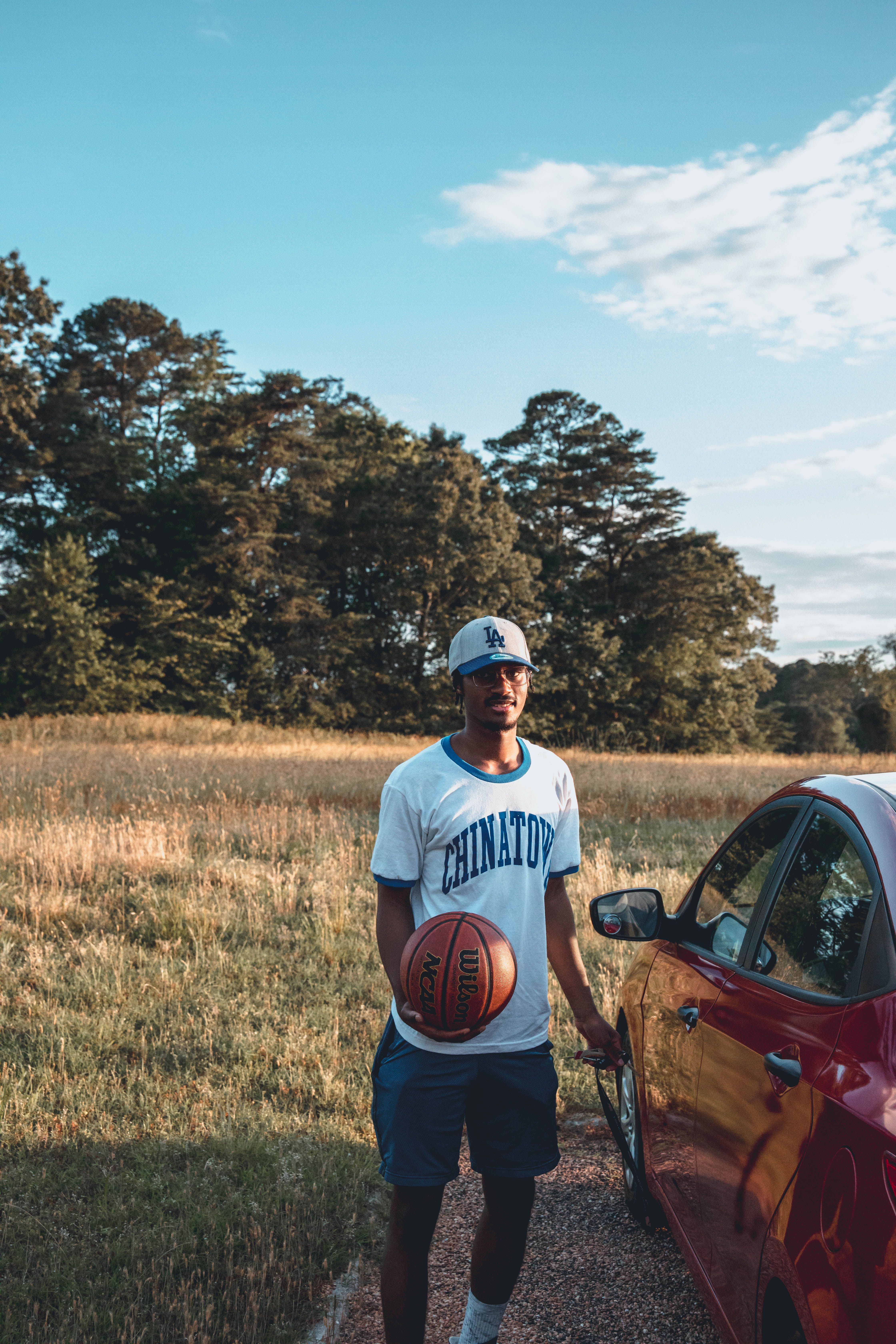 Young African American basketball player in sportswear in picturesque scenery of countryside near vehicle under bright sky