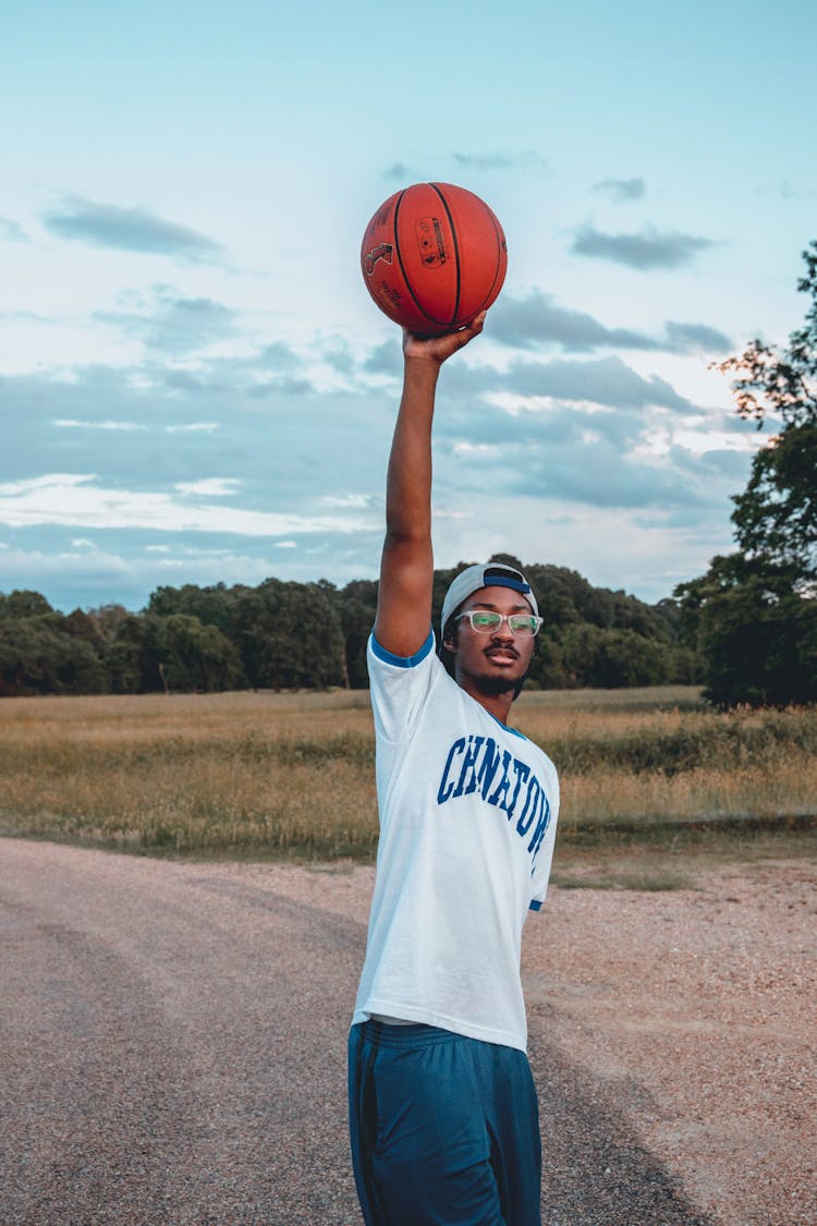 Black Sportsman With Basketball On Roadway Under Cloudy Sky