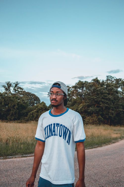 Free Young pondering African American guy in sportswear and eyeglasses looking away on roadway under cloudy sky in countryside Stock Photo