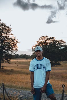 Brutal young African American male in casual clothes standing in solitude in countryside terrain and looking at camera