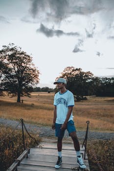 Young man in casual attire enjoying a peaceful outdoor setting on a wooden bridge.