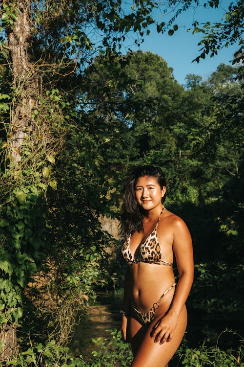 Smiling young ethnic female in bikini resting in green vegetation