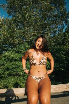 Young Asian tanned female in swimsuit enjoying hot summer vacation in sunny garden with lush green trees