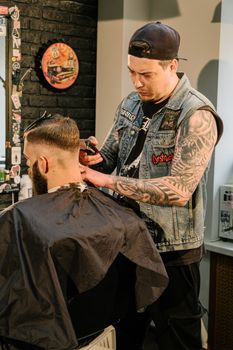 A tattooed barber skillfully styles a client's hair in a trendy salon, showcasing modern men's grooming.