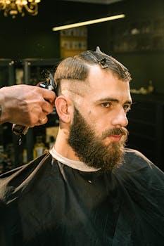 A man receives a haircut and trim in a professional barbershop setting with focus on style and detail.