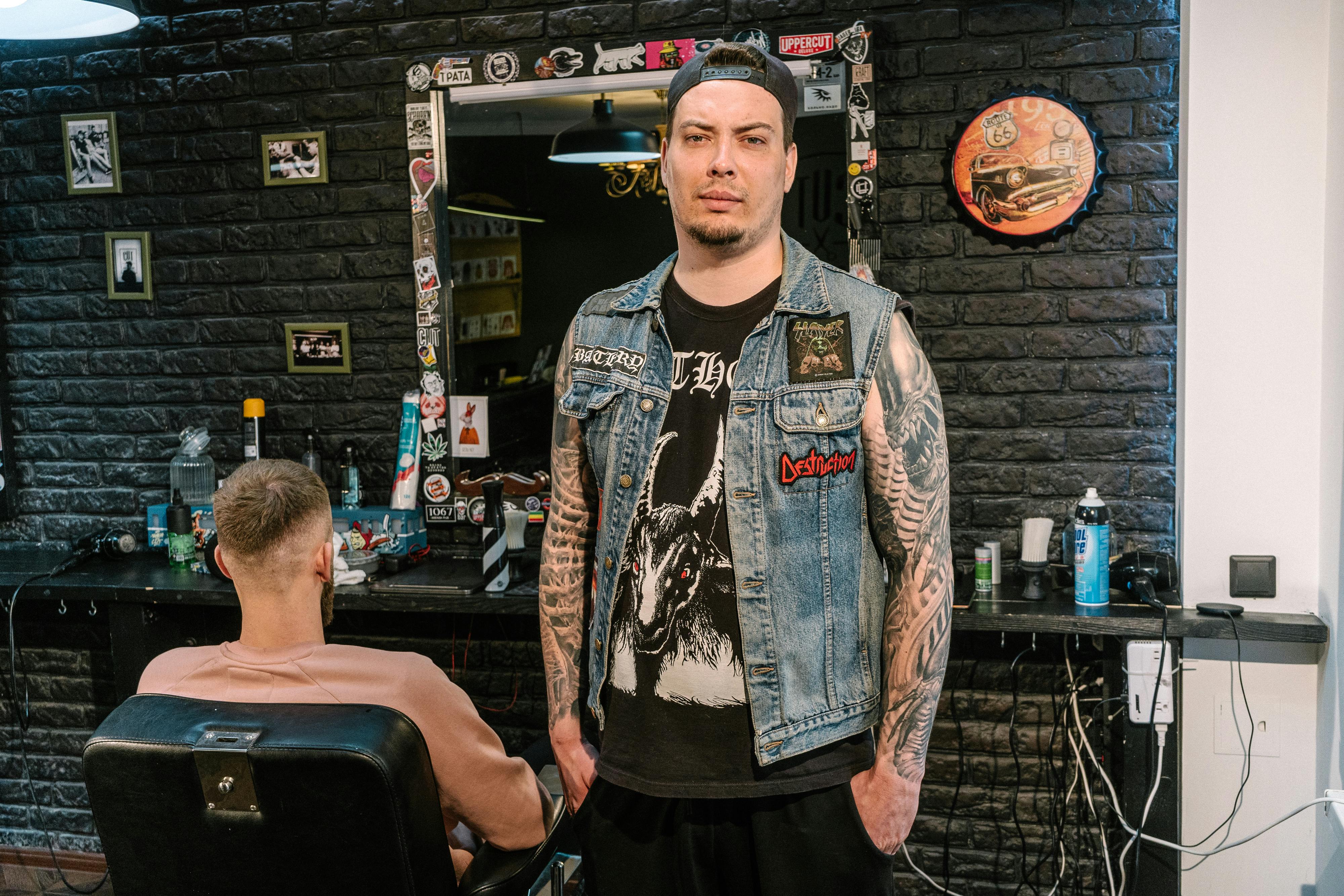 A tattooed barber stands in a trendy barbershop, showcasing style and personality.