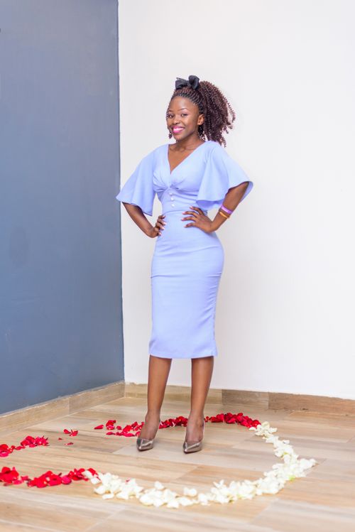 Free Full body stylish African American female in classy blue dress standing with hands on waist on floor in heart made with rose petals and looking at camera with toothy smile Stock Photo