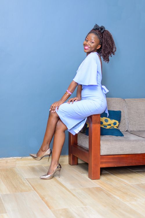 Free Side view full length elegant African American female wearing chic blue dress sitting on cozy couch arm and looking at camera happily Stock Photo