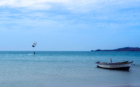 Amazing view of distant kite surfer practicing on blue sea near moored old boat in peaceful resort