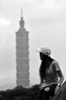 一位年轻女子坐在山顶上，在单色环境中眺望台北101