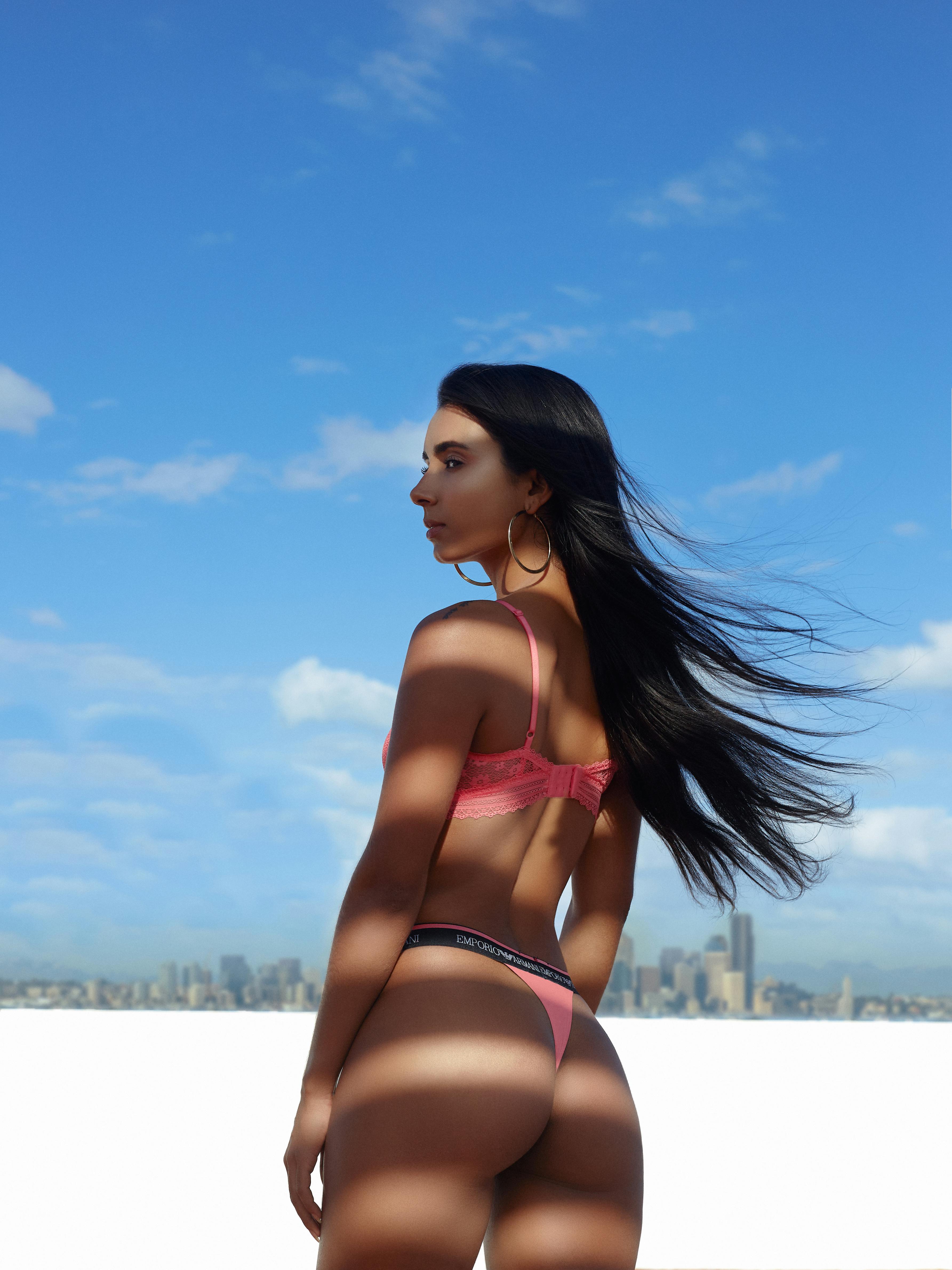 Fashion model posing in pink lingerie against urban skyline backdrop.