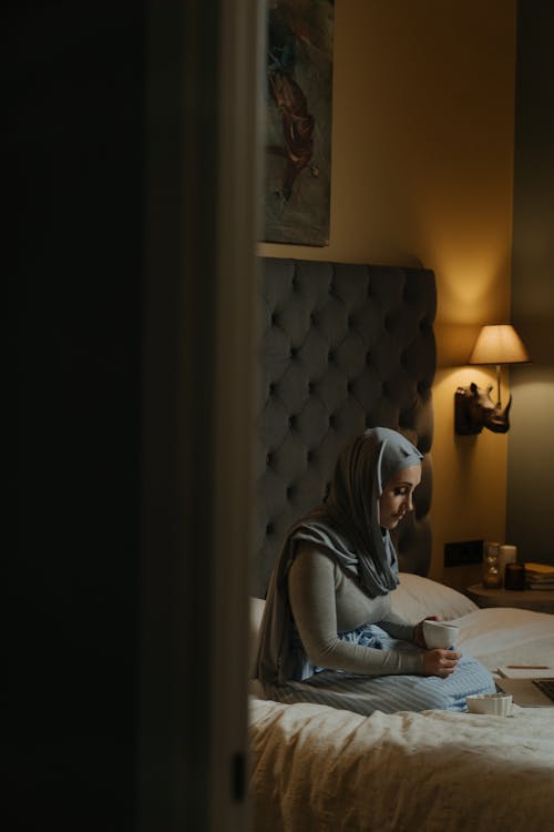 灰色蓋頭的女人坐在床上使用筆記本電腦