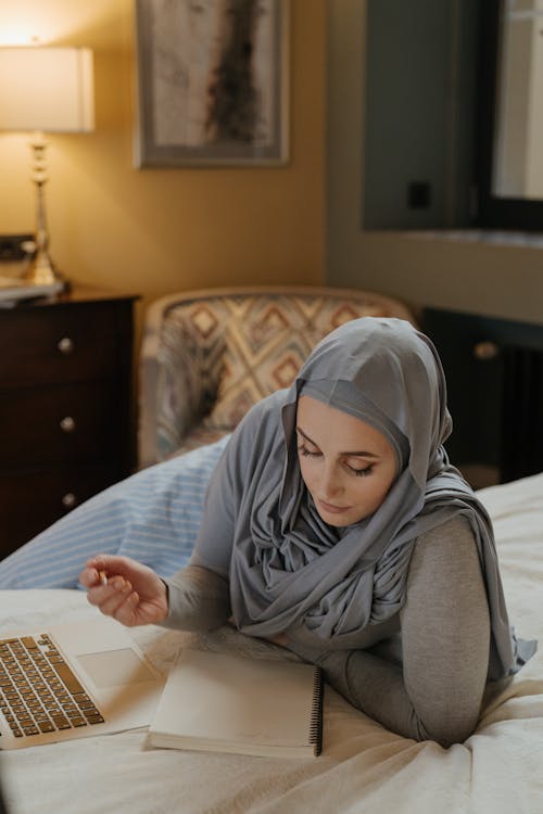 Vrouw In Grijze Hijab Notities Maken Tijdens Het Gebruik Van Laptop