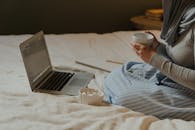 一位女士在床上远程工作，带着笔记本电脑、茶和记事本