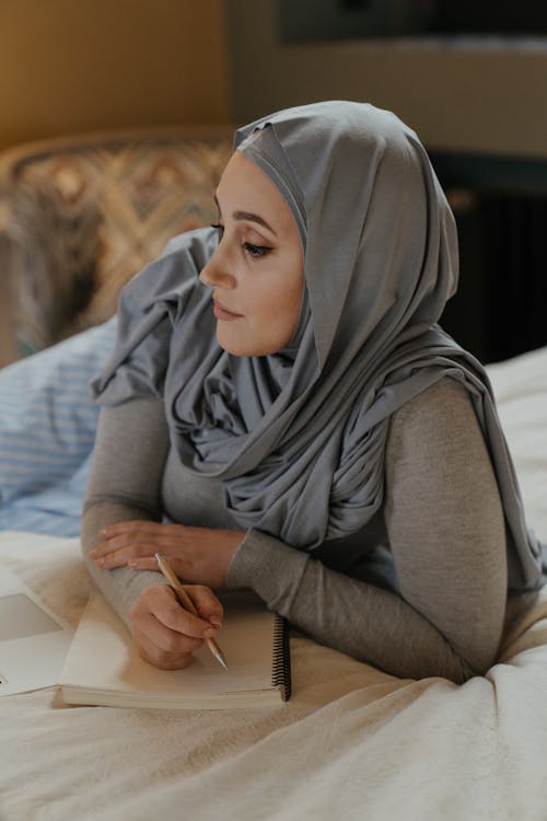 Женщина в сером хиджабе сидит на диване
