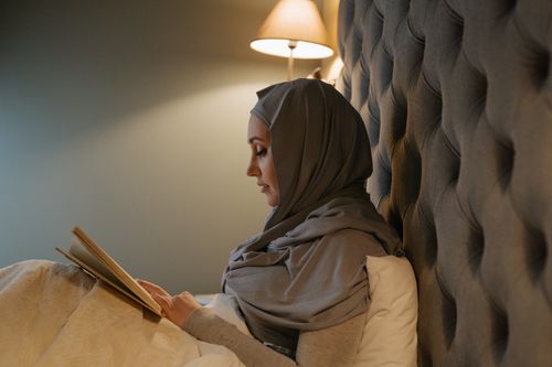 Free A woman in traditional attire reading in a cozy bedroom setting, highlighting relaxation and cultural identity. Stock Photo
