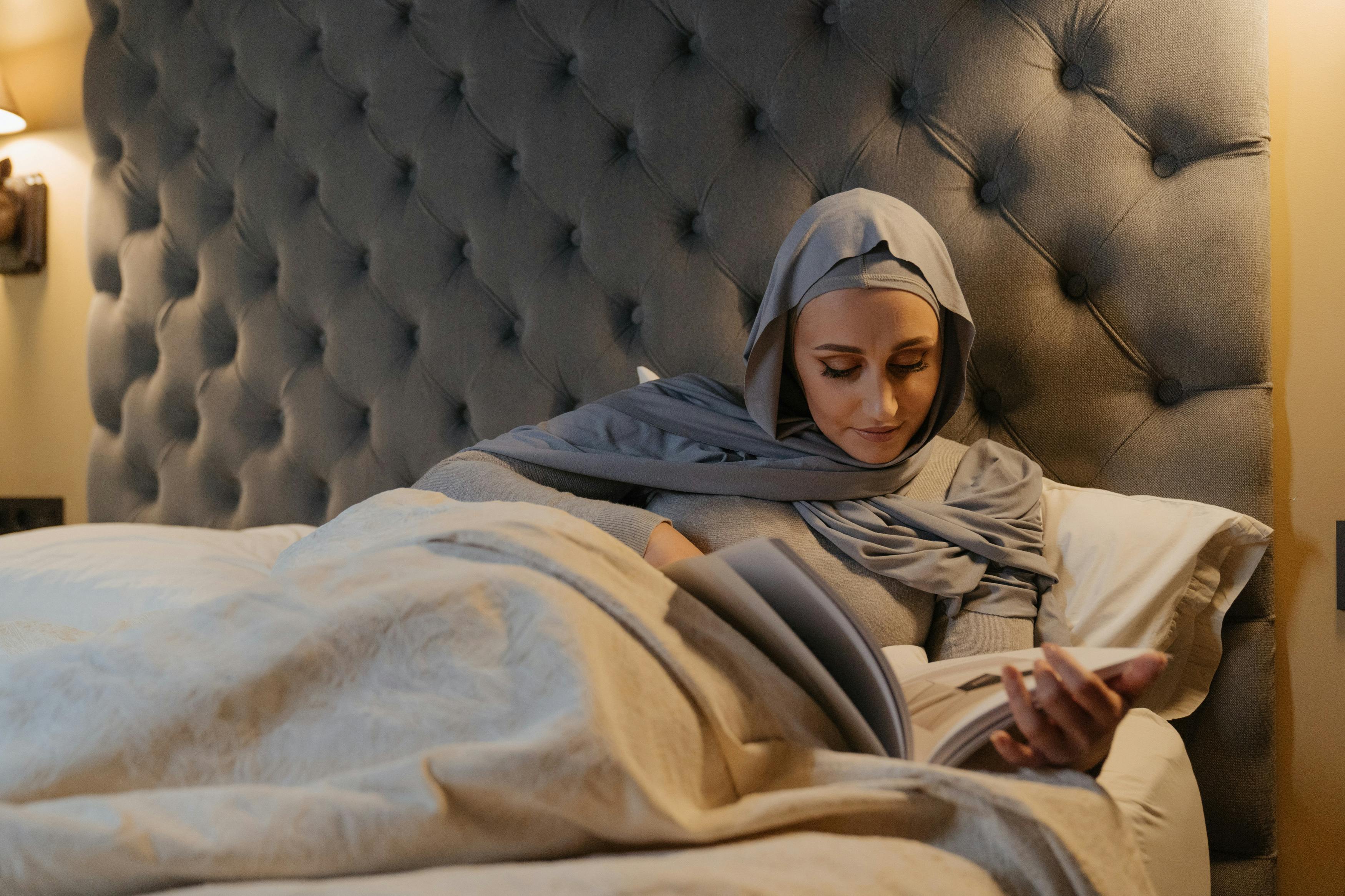 private riviera maya cultural tours booking - A woman in traditional Islamic attire reads a book while relaxing in bed.