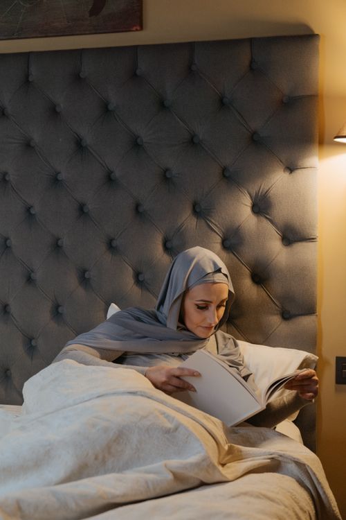 Free A Muslim woman wearing traditional clothes relaxes and reads in a cozy bedroom setting. Stock Photo