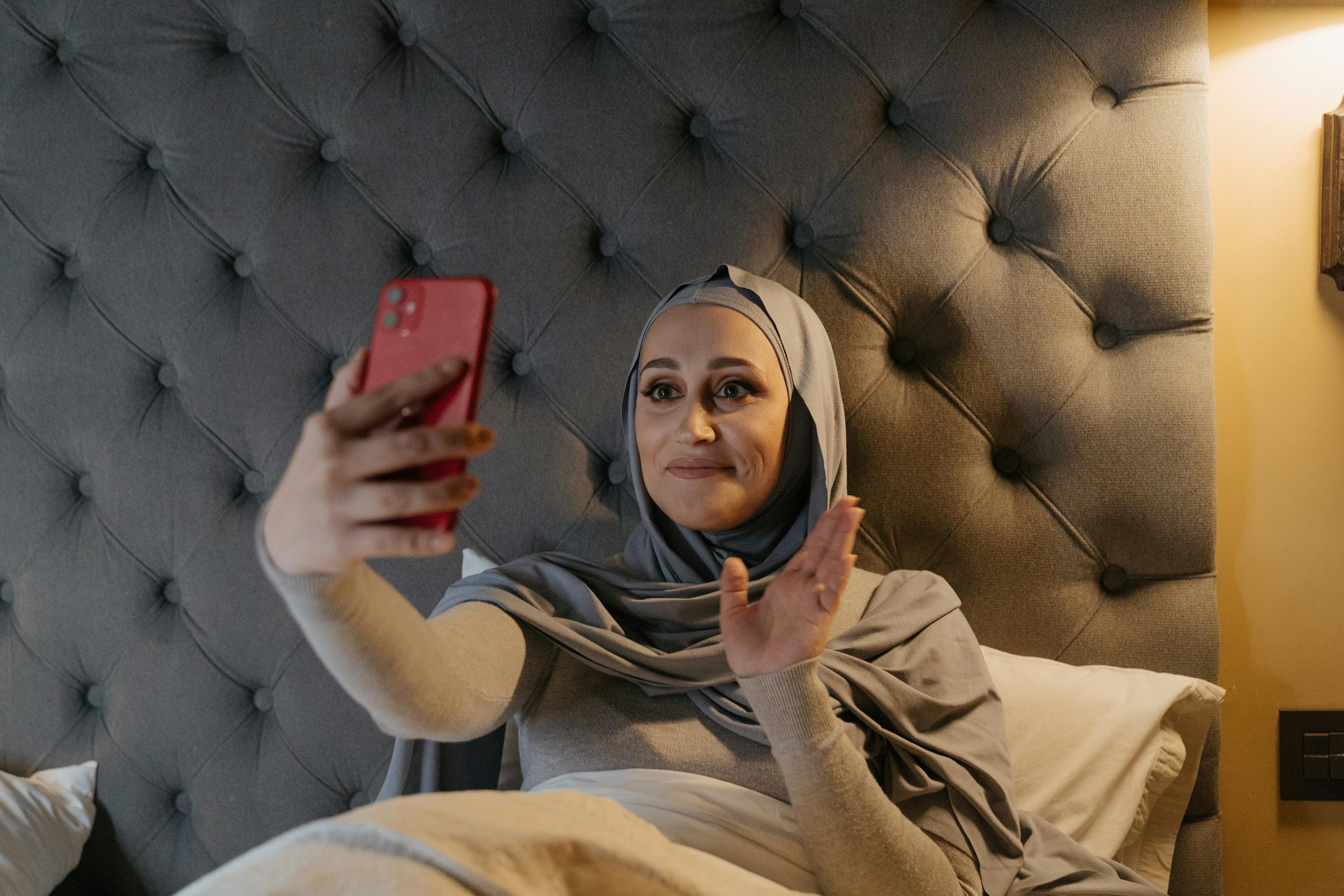 woman in brown hijab holding red smartphone