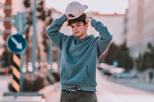 Free Young trendy male teenager in hoodie with cap standing with raised arms and looking at camera in town Stock Photo