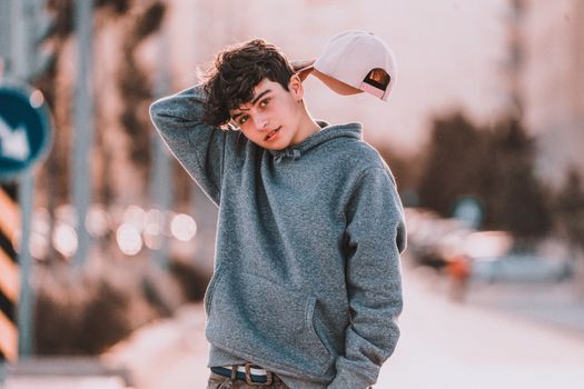 Contemplative teenager in stylish apparel with raised arm standing with tilted head on street while looking at camera